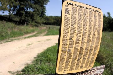 Табличка «Park Rules and Regulations» с мелким плотным текстом у грунтовой дороги