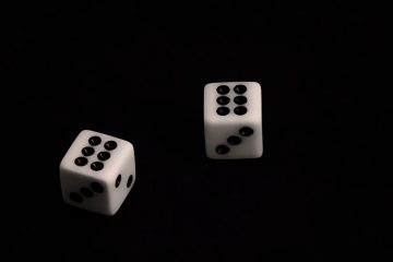 Два белых игральных кубика с чёрными точками на тёмном фоне
